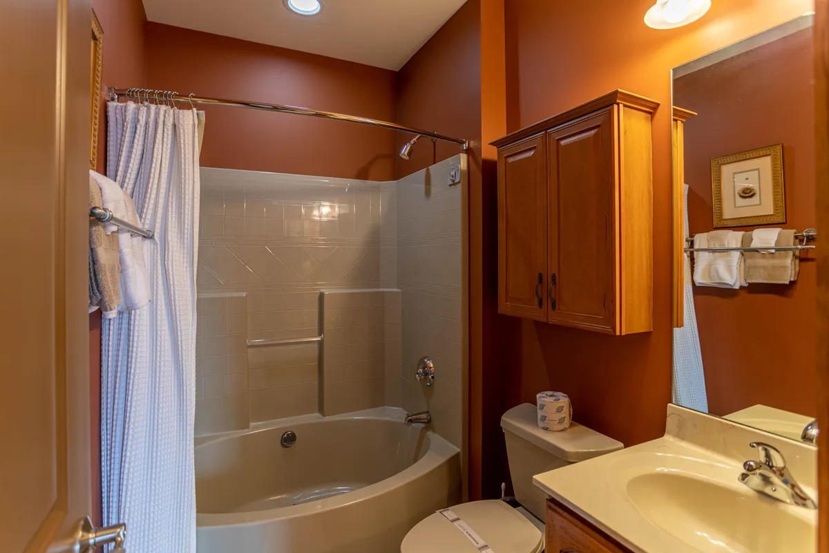 A calm bathroom scene featuring a luxurious bathtub, wooden cabinetry, and a mirror. The space is designed for relaxation, ideal for unwinding at the end of the day or preparing for a gentle morning.
