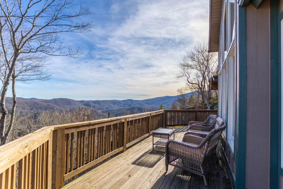 A spacious wooden deck overlooking expansive mountain vistas. The outdoor seating arrangement invites relaxation and social interaction, while the panoramic view of the mountains provides a stunning natural backdrop. The deck is situated high above the surrounding landscape, ideal for gatherings or peaceful moments spent appreciating the scenery.