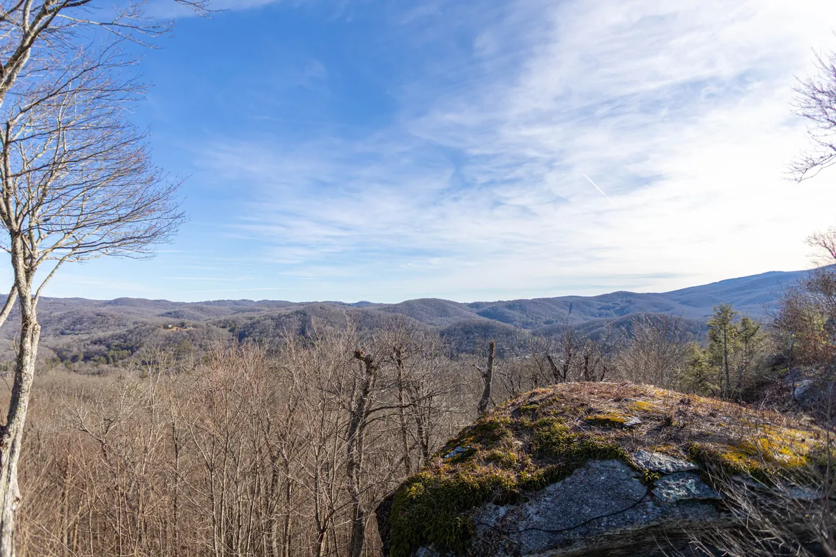 A breathtaking mountain range stretches across the horizon, with rocky outcrops and bare trees in the foreground. The early morning light casts a tranquil glow over the landscape, inviting exploration and outdoor adventure.