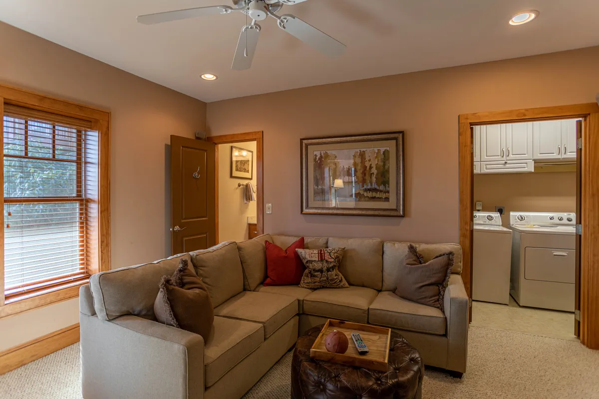 A cozy interior space featuring a comfortable sofa, coffee table, framed artwork, and a visible laundry area to the side. The TV is set up conveniently for viewing from the couch, making it ideal for both relaxation and entertainment. Soft lighting and inviting decor create a welcoming and practical atmosphere.