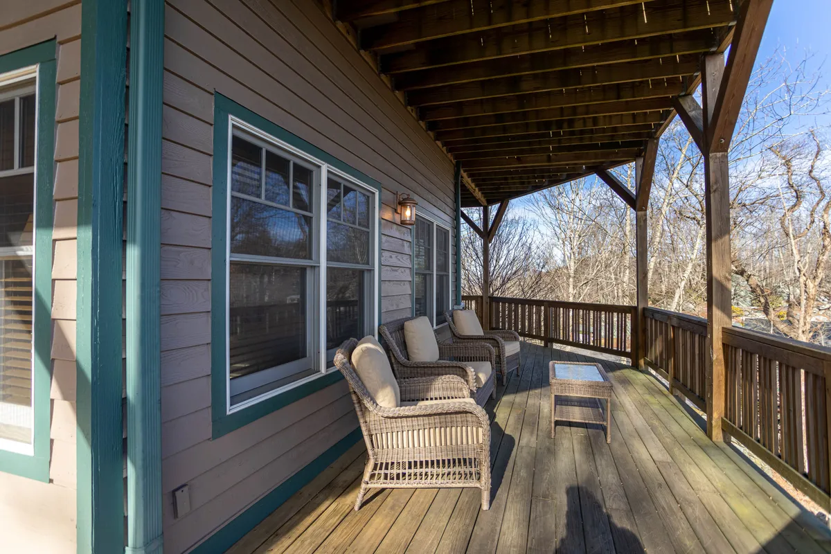 This exterior shot features a tranquil mountain deck outfitted with wicker chairs and a coffee table, bordered by a wooden railing. The vantage point allows for serene views out over the surrounding landscape, suggesting a perfect spot for morning coffee or evening relaxation while soaking in mountain vistas.