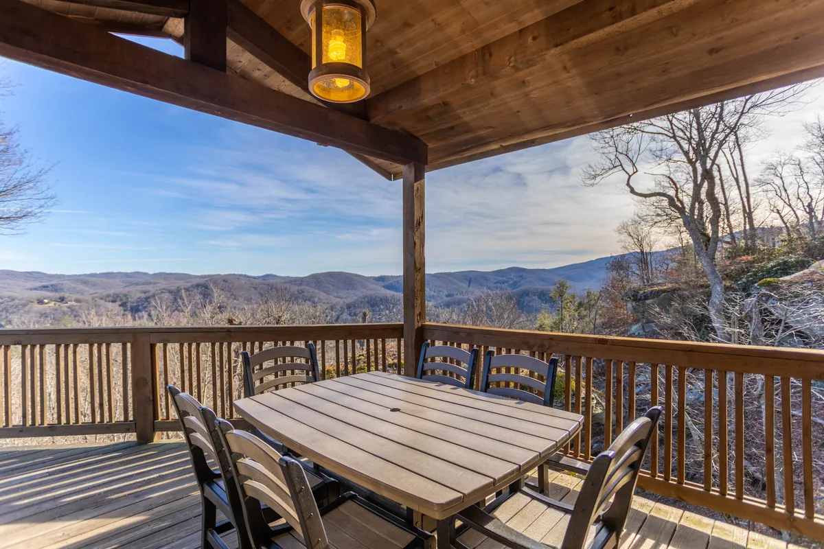 An inviting exterior deck scene with a sturdy wooden dining table, matching chairs, and a hanging lantern. The panoramic mountain view serves as a breathtaking backdrop, reinforcing the connection to nature and the deck’s suitability for both lively gatherings and tranquil moments.