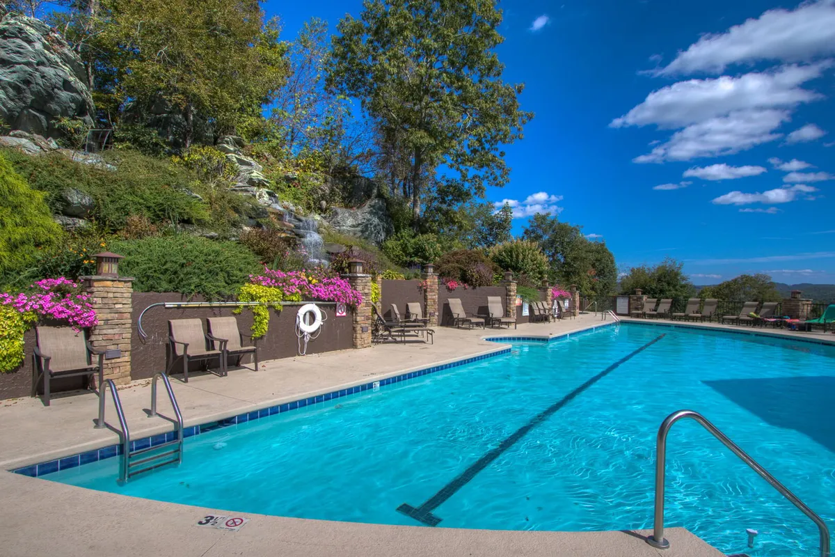 An inviting outdoor swimming pool is nestled within a beautifully landscaped garden. The scene includes lounge chairs, vibrant flowers, and a gentle waterfall, all set beneath open skies—providing a tranquil yet active community gathering space.
