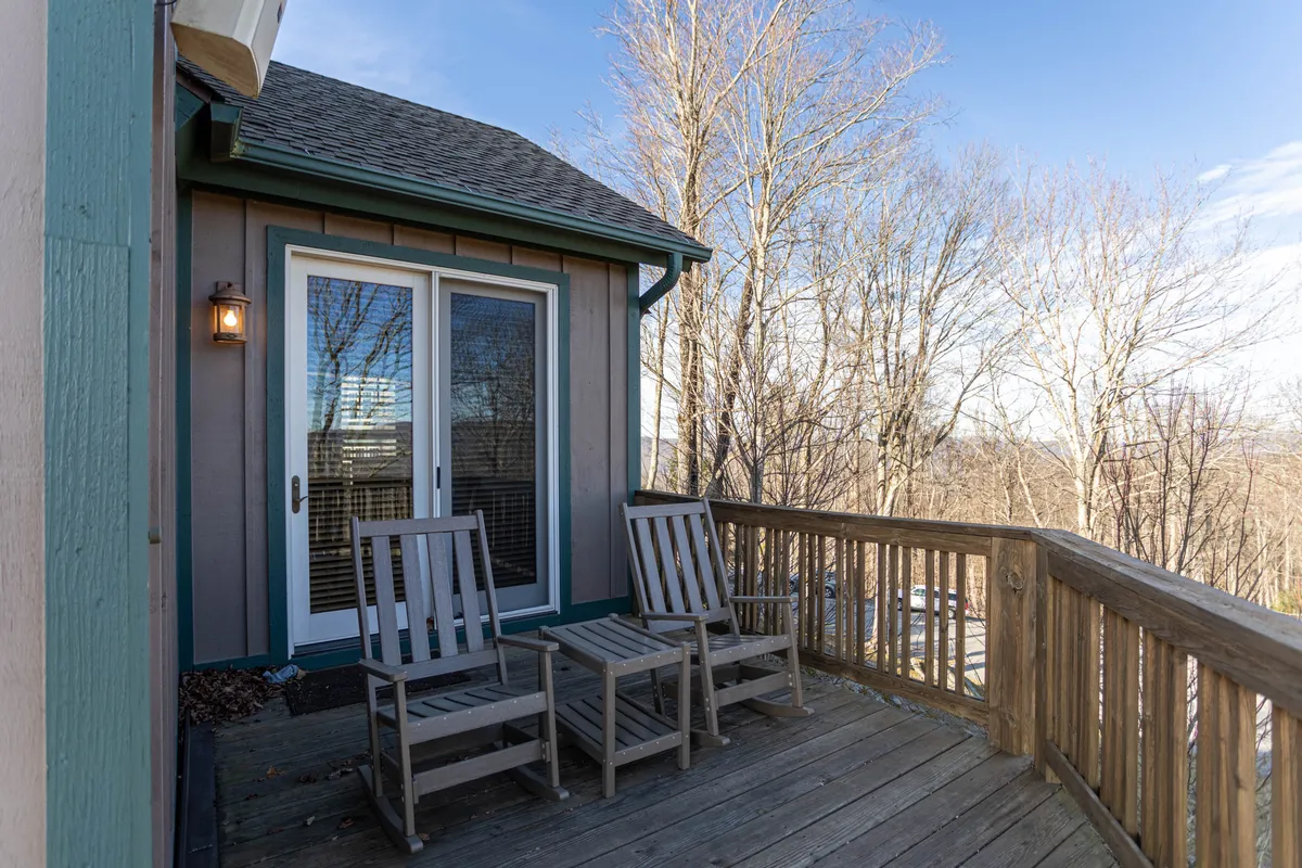 This image features a pair of wooden rocking chairs set on a welcoming porch, framed by double doors and lush surrounding trees. The porch offers a calm and peaceful space to relax outdoors, blending seamlessly into the natural landscape around the property.